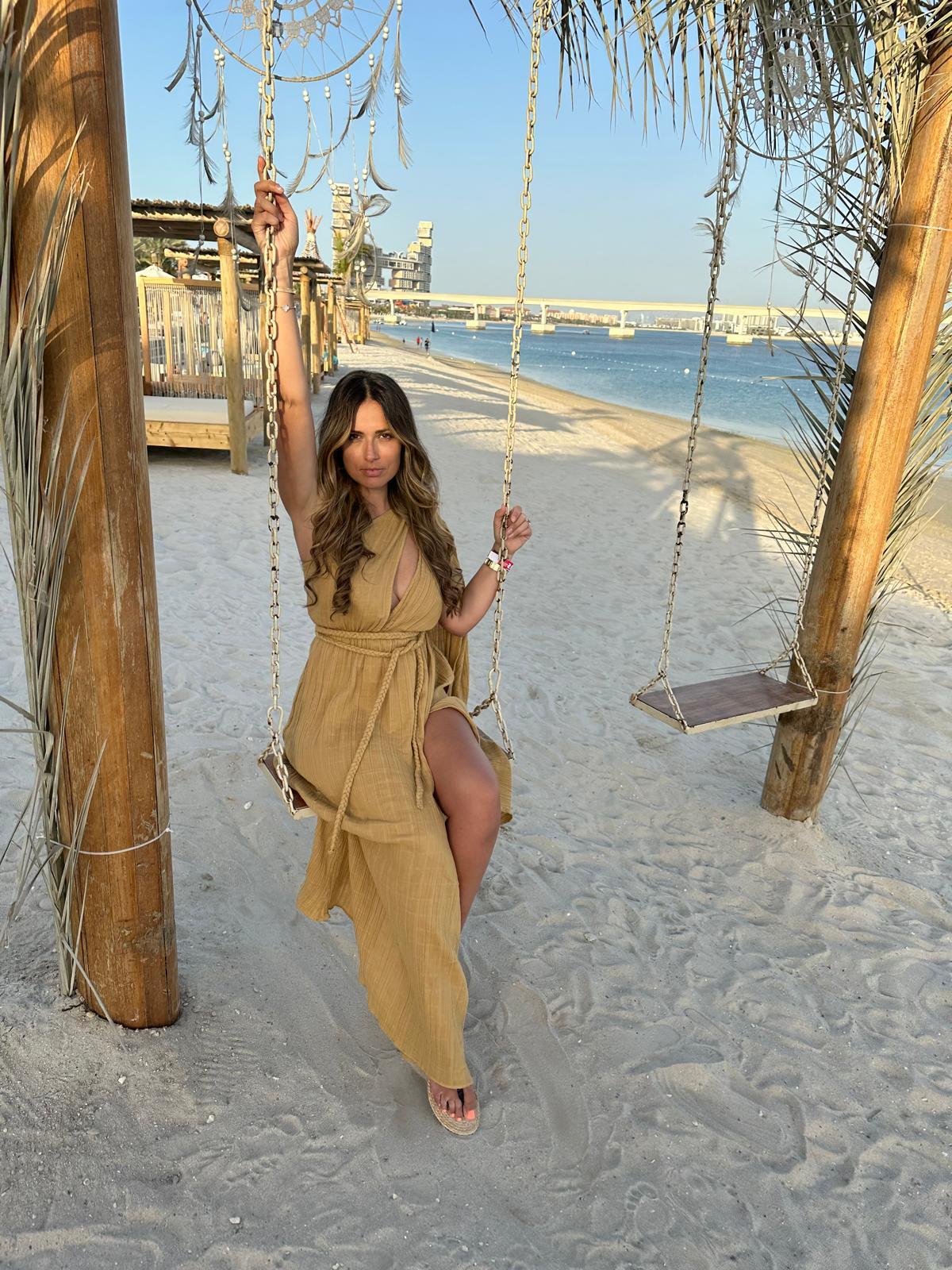 image of rachel buscall in a earth tones dress on swing by the ocean